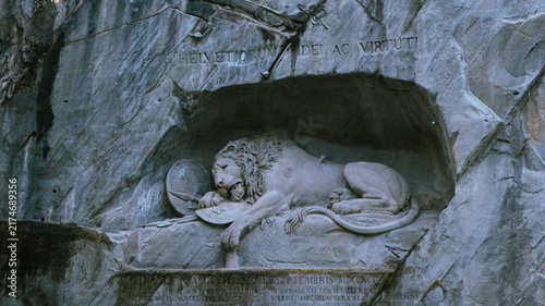 Фотография A detailed shot of the historic Lion Monument rock-cut sculpture showing a dying lion carved into a stone cliff with Latin inscriptions