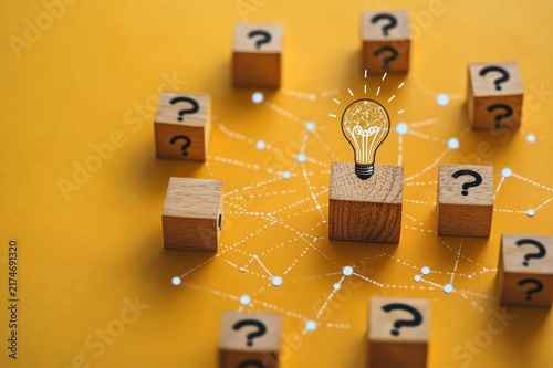 wooden blocks with question marks on a yellow background linked by dotted network and a central block topped by a glowing light bulb showing hopeful creative insight