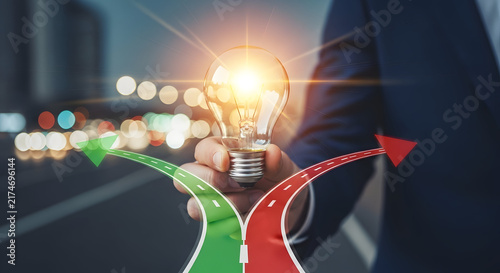Businessman holding glowing light bulb with split direction road signs for innovation and strategy