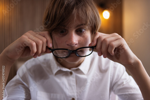 Quadro su tela Teenager boy with wide-eyed, surprised expression holding his eyeglasses in his