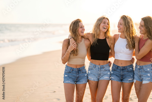 Young women friends laughing together at beach during golden hour