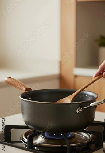 Healthy home cooking and culinary preparation, person stirring food in a nonstick saucepan on a gas stove in a modern kitchen with wooden accents
