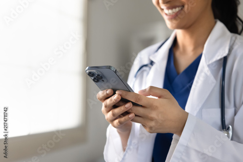 Cropped closeup view of South Asian female doctor texting on smartphone in clinic. Digital communication in healthcare, telemedicine application use, remote medical consultations of patient concept