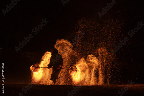 Obraz na plátně Silhouette performer creating fire sparks during traditional night performance