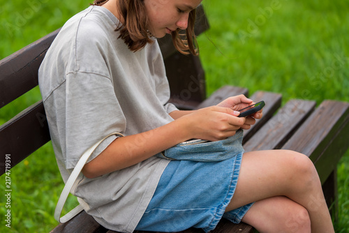 Cuadro en lienzo Teenage girl focuses on her phone while sitting on a bench