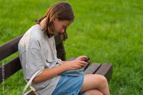 Obraz na płótnie Teenage girl focuses on her phone while sitting on a bench