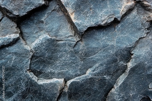 Close-up of dark cracked stone surface with jagged fissures and rough weathered texture conveying ancient, austere solidity