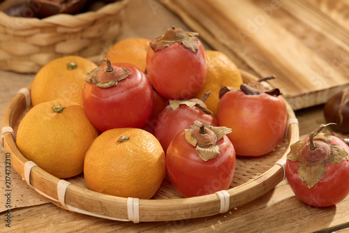 Persimmons and Oranges in a Basket on a Wooden Table