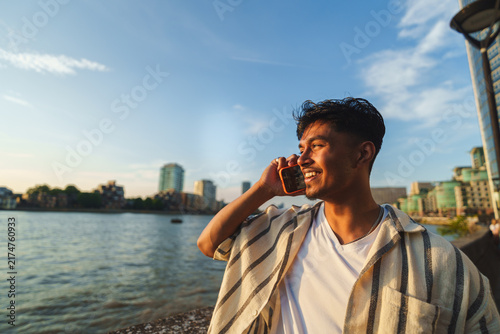 Photography Young man smiling and talking on his mobile phone by the river thames at sunset