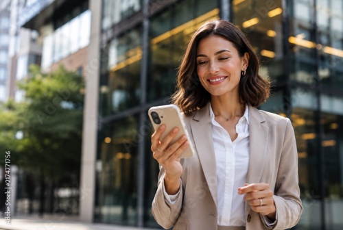 Happy Professional Woman Using Mobile Phone Against Modern Office Buildings