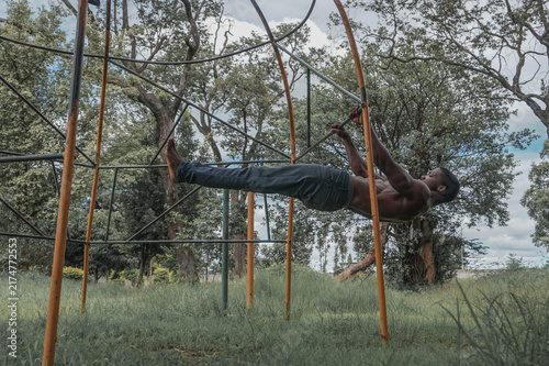 Fotografie Shirtless muscular African man performing a front lever calisthenics exercise on an outdoor playground jungle gym