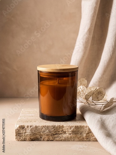 Blank amber glass scented candle jar mockup with wooden lid on travertine stone plinth with linen drape