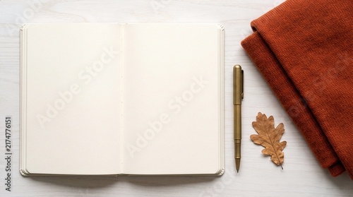 Open blank notebook mockup with brass pen folded knit scarf and dry autumn oak leaf on white wood desk