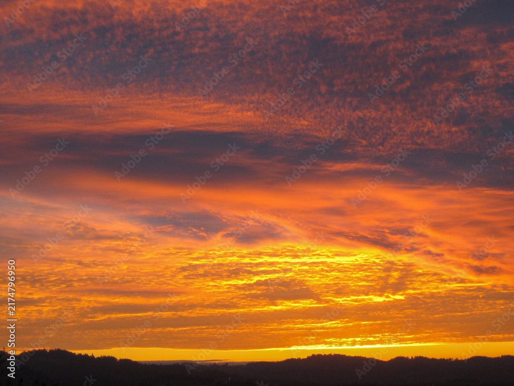 Fototapeta premium Fiery Orange Sunset Beneath Dramatic Textured Clouds