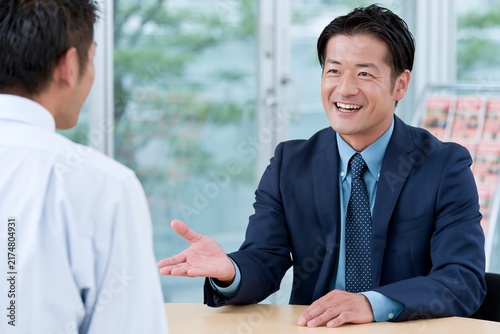 オフィスで笑顔の日本人ビジネスマンが商談相手に説明提案