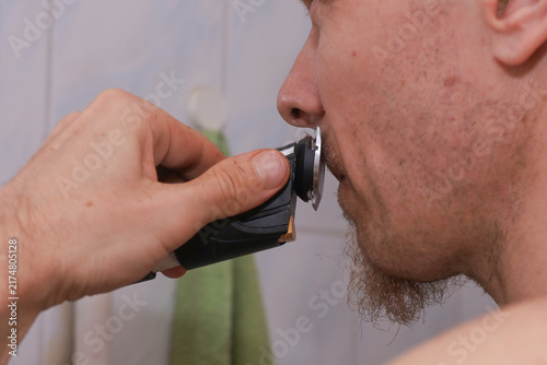 Foto Man using electric shaver for facial grooming in bathroom