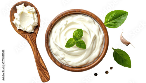 Creamy dip is presented with basil leaves in a wooden bowl next to a spoonful of more dip and garlic