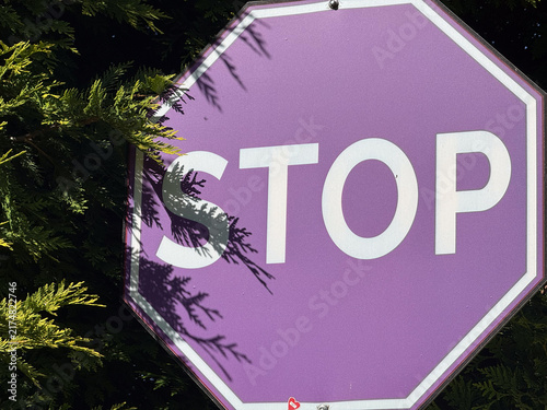 close up purple stop sign against green bushes, sunny day, concept of safety, traffic, warning, banner