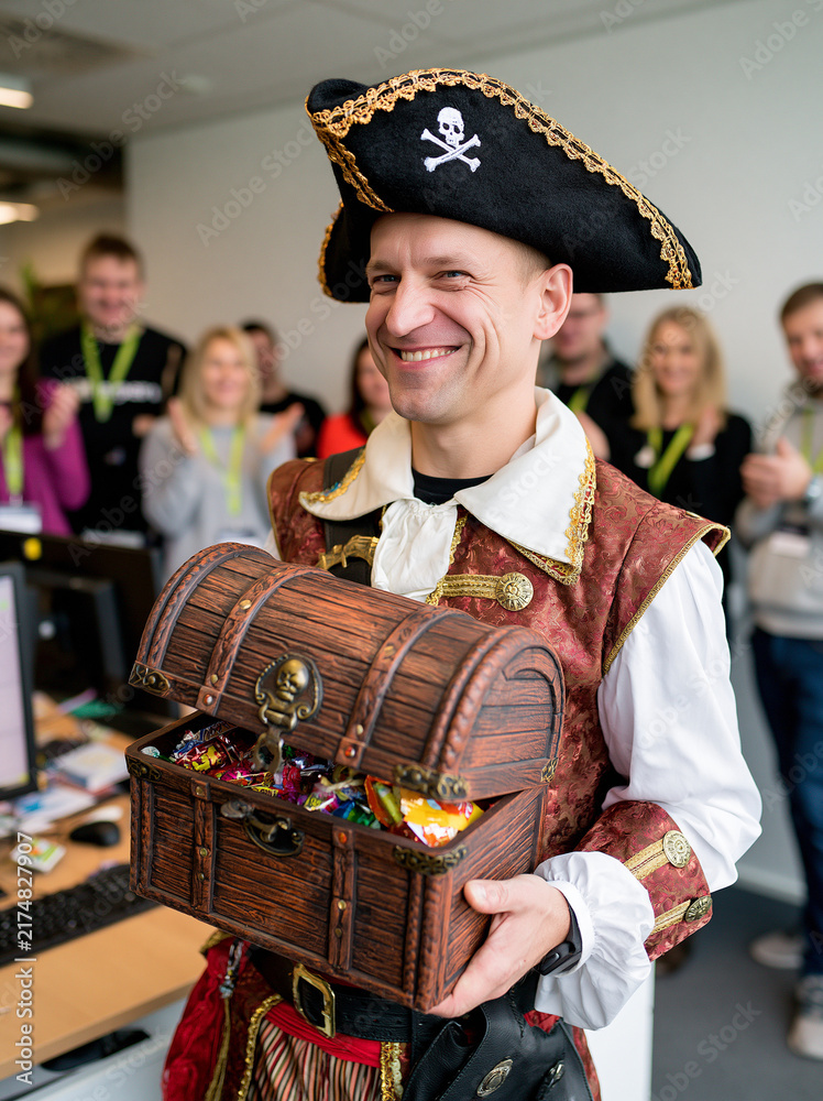Fototapeta premium Man in pirate costume and tricorn hat holding treasure chest filled with candies for Halloween