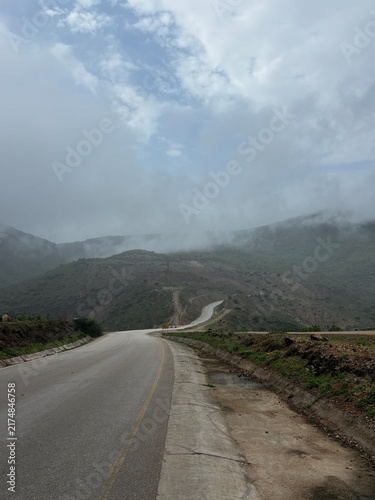 Scenic road in Salalah, Oman, winding through the lush green Dhofar Mountains during Khareef season, with misty hills, cloudy skies and beautiful natural surroundings. the gulf country near to Kerala