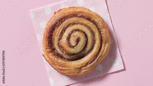 Top view closeup of sweet cinnamon bun rotating on a pink napkin against pink background. Colorful sweet pastry  in a playful composition
