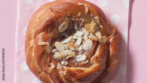 Top view closeup of sweet caramel bun rotating on a pink napkin against pink background. Colorful sweet pastry with almond  in a playful composition