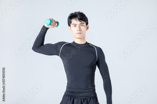 Young man lifting dumbbell during shoulder workout in studio