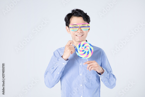 Smiling young man with colorful novelty glasses and swirl lollipop in studio