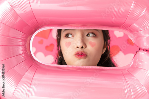 Photography Playful young woman framed by pink balloon with heart makeup on pink background