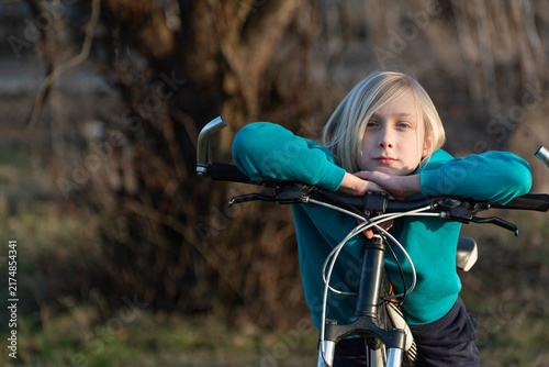Konstfotografi Blonde child leaning on bicycle handlebars, gazing calmly at camera with relaxed