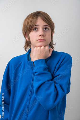 Fotografie Young boy in a blue jacket looking upwards, resting his chin on his hand, displa