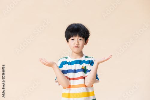 Bild auf Leinwand Confused young boy shrugging with helpless expression on beige background