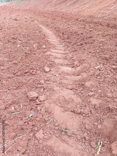 Deep tractor tire tread mark in dry red clay soil on agricultural land.