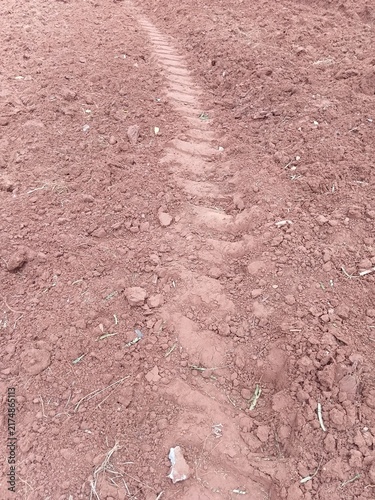Deep tractor tire tread mark in dry red clay soil on agricultural land.