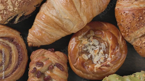 Top view closeup of assortment of freshly baked sweet pastries and buttery croissants, caramel bun, slowly rotating on dark wooden background. Delicious bakery selection for commercial use