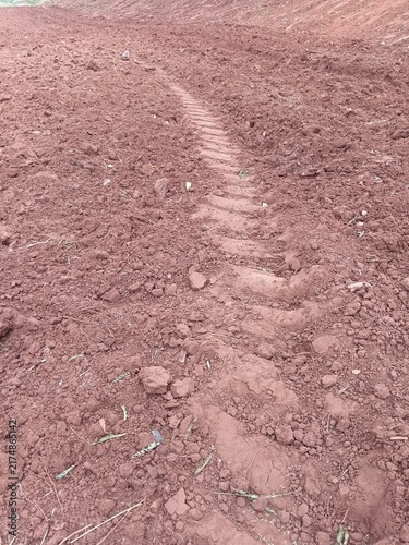 Deep tractor tire tread mark in dry red clay soil on agricultural land.
