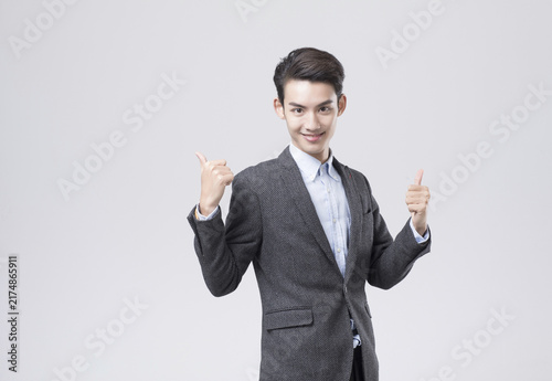 Obraz na płótnie Smiling young businessman giving two thumbs up in studio