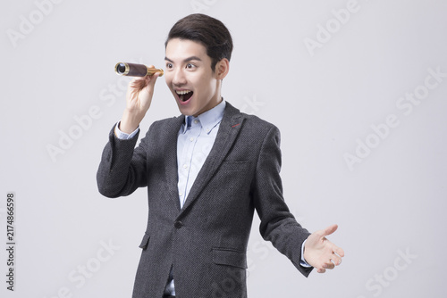 Foto Excited young businessman looking through a spyglass in studio