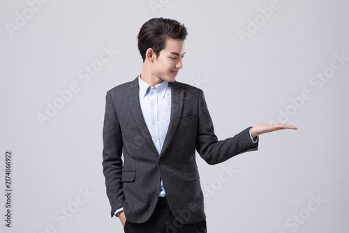 Young businessman presenting with open palm on gray background