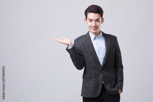 Young businessman presenting with open hand on gray background