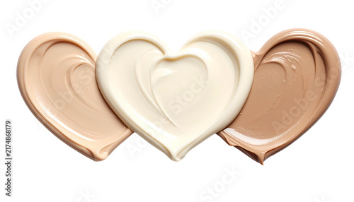 Three heart-shaped swatches of various shades of cosmetic cream or foundation, displayed against a black background