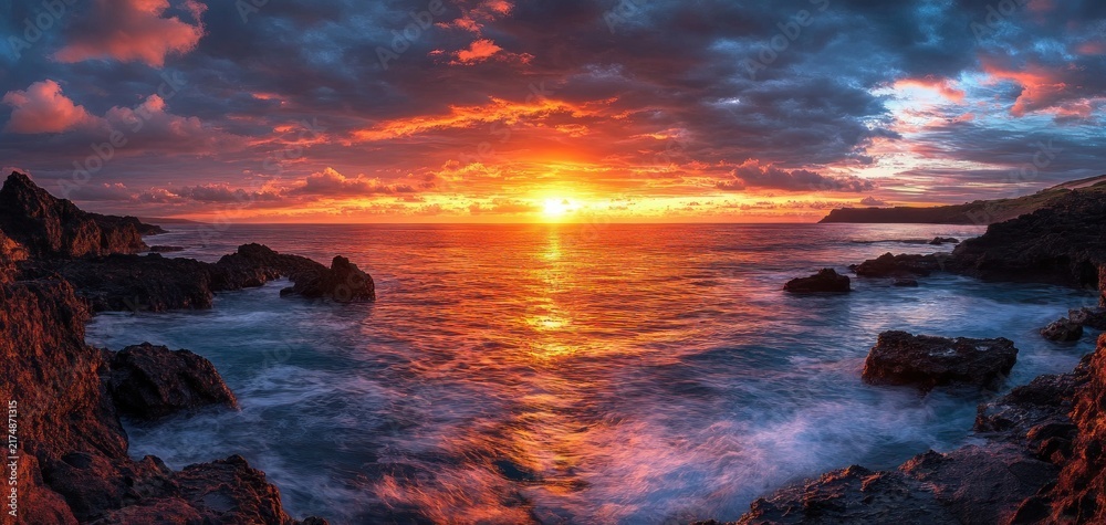 Fototapeta premium Fiery sun setting over a rocky coastline with dramatic clouds, glowing ocean reflections and crashing waves, evoking awe and tranquility