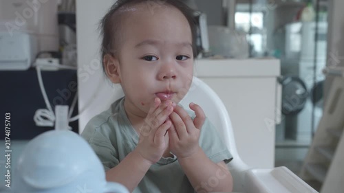 A cheerful toddler is sitting in a high chair, clapping their hands with a playful expression. The background features a modern kitchen setting, suggesting a cozy environment for mealtime moments.