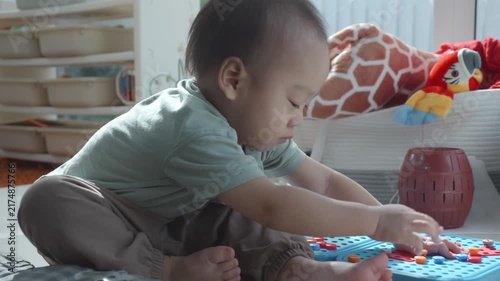 A young child sits on the floor, focused on playing with colorful building blocks, surrounded by toys in a cozy indoor environment. This scene captures the joy of childhood creativity and exploration.