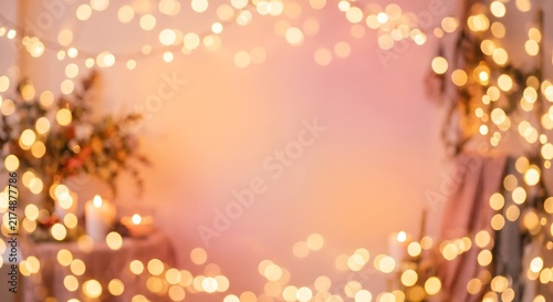 Golden bokeh lights with glowing garland and candles on soft pink background. Cozy festive interior backdrop for holiday, wedding, birthday, valentines day and celebration design.