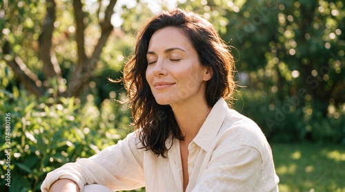 A peaceful young woman with her eyes closed sitting calmly in a sunlit green garden with outdoors lush garden closed gentle smile