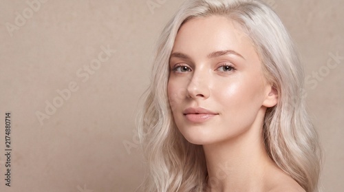 Portrait of a beautiful woman with long blonde wavy hair posing against a neutral beige background looking at camera
