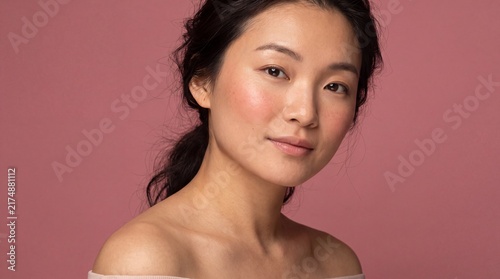 Portrait of a young asian woman with natural makeup posing against a plain pink background with gentle expression natural