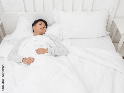 Young man sleeping peacefully in white bed at home