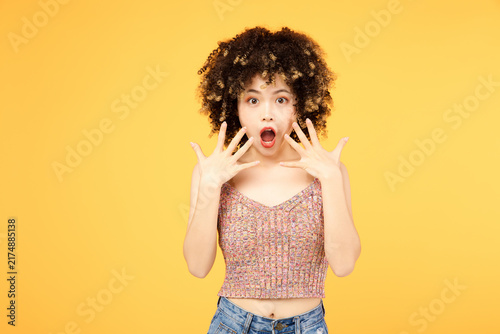 Obraz na płótnie Surprised young woman with curly hair reacting on yellow background